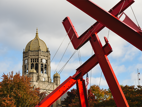 Bright red modern sculpture Victors Lament stands in the foreground, with the historic Haas clocktower in the distance.